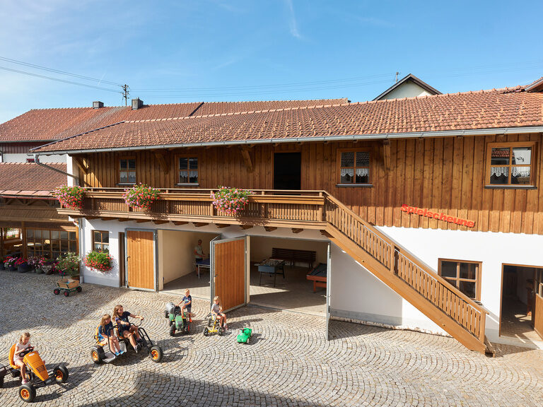 Eine Gruppe Kinder spielt bei traumhaftem Wetter im Hof des Familienbauernhofs.