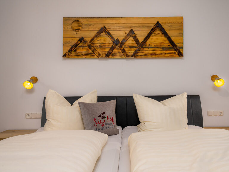 Im Familienbauernhof Süßhof steht ein gemütliches Bett, über dem ein kunstvolles Holzbild für eine warme Atmosphäre sorgt.